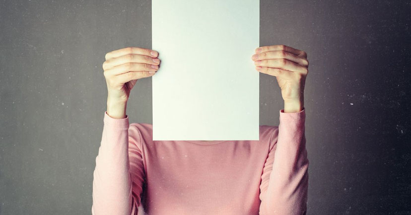 Eine Frau verdeckt ihr Gesicht mit einem weißen Blatt – Sinnbild für innere Blockaden, Selbstbild und die Frage: Warum stehe ich mir selbst im Weg?