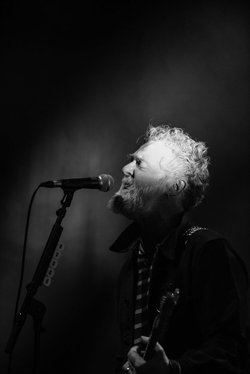 Black and white photo of Glen Hansard singing into a microphone, head tilted back, performing at L'Olympia Paris.