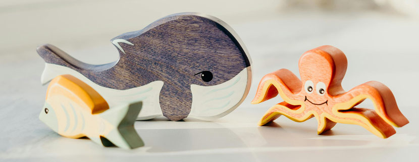 Spielfiguren aus Holz vorne links ein kleiner Fisch, dahinter ein großer Wal und daneben rechts ein orangefarbener Tintenfisch