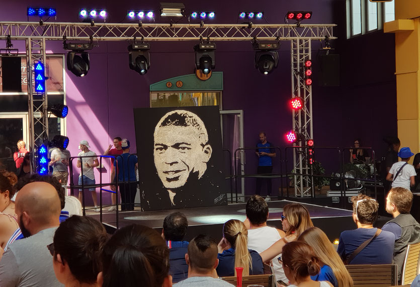 Portrait glitter painting de Kilian MBappé par le peintre performer EriK Black sur la scène du sports bar. Coupe du monde 2018