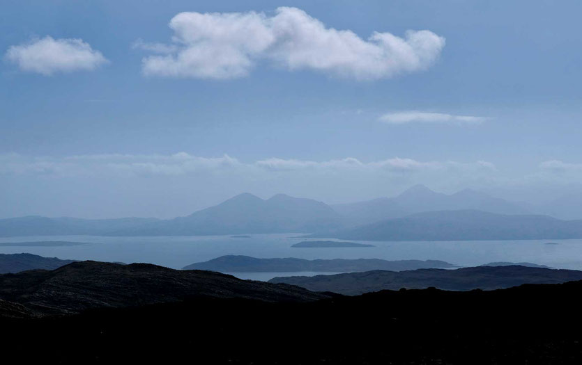 Von der Passhöhe blicken wir die Serpentinen hinunter, hinter uns im Westen die Bergkette der Isle of Skye.