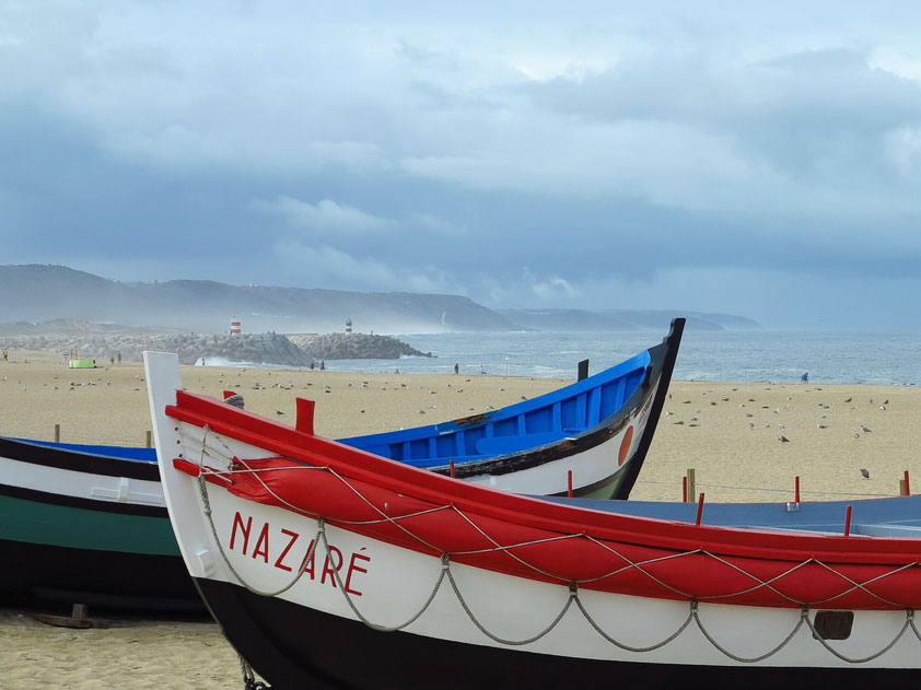 Alte Fischerboote am Sandstrand von Nazaré. Früher wurden diese Boote von Ochsen auf den Strand gezogen.