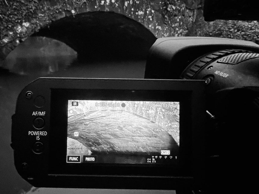 Eine Infrarot-Videokamera filmt eine alte Steinbrücke über Wasser. Auf dem Kameradisplay ist das Brückenmauerwerk in Infrarotdarstellung zu sehen.