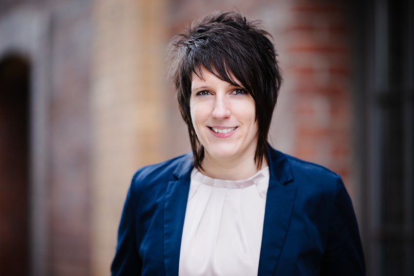 Bewerbungsfoto einer lächelnden jungen Frau mit kurzen dunklen Haaren und blauem Blazer.