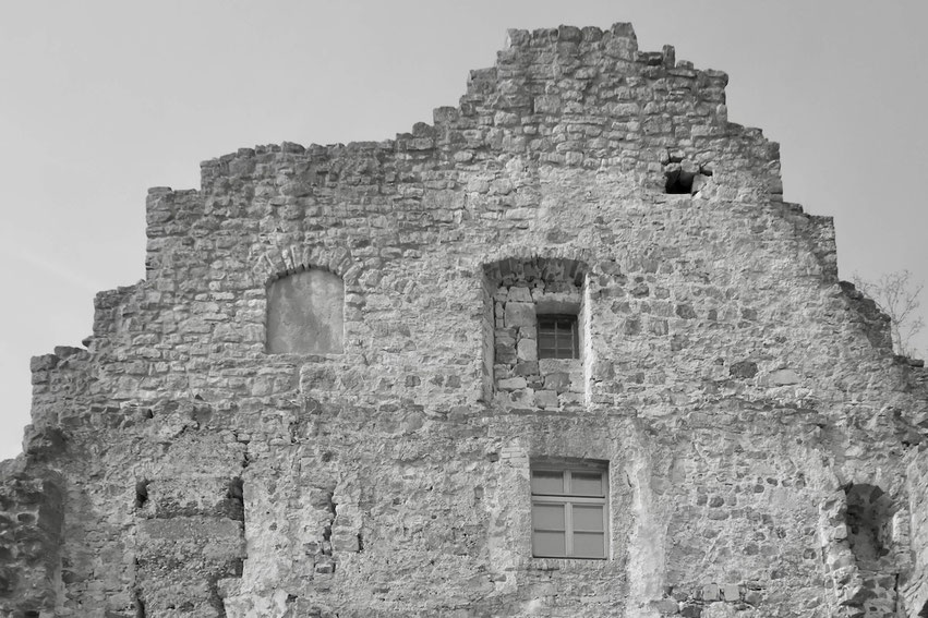 Ein detailreicher Blick auf die Ruine Lichtenburg in Ostheim vor der Rhön, die trotz ihrer Verfallszeit die beeindruckende Handwerkskunst vergangener Epochen offenbart. Das Schwarz-Weiß-Foto betont die Beständigkeit der Steinmauern.