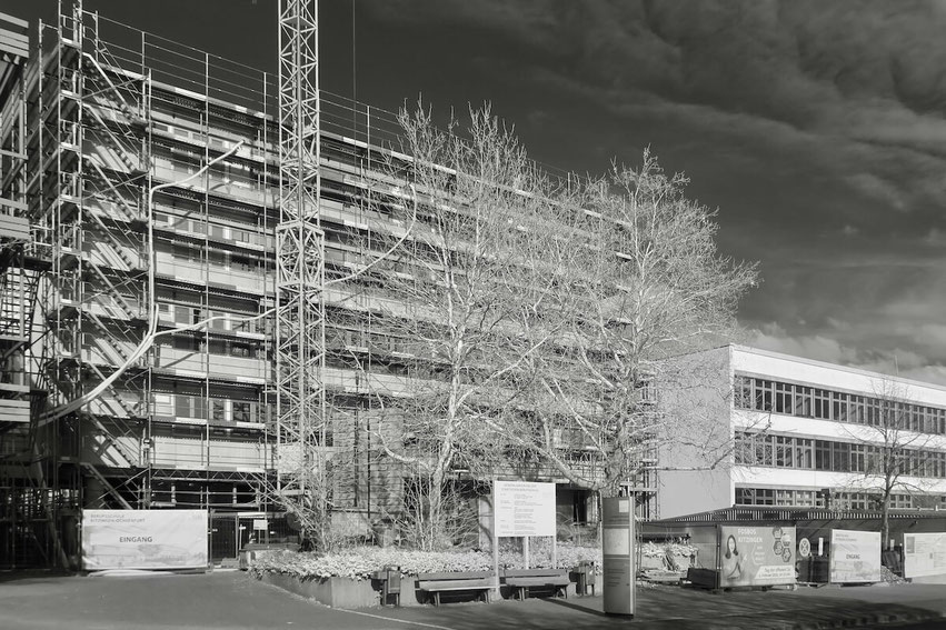 Das Bild zeigt eine moderne, zweistöckige Schule mit einer klaren, rechteckigen Architektur. Die Fassade ist hell und weist große Fenster auf. Der Himmel ist leicht bewölkt.