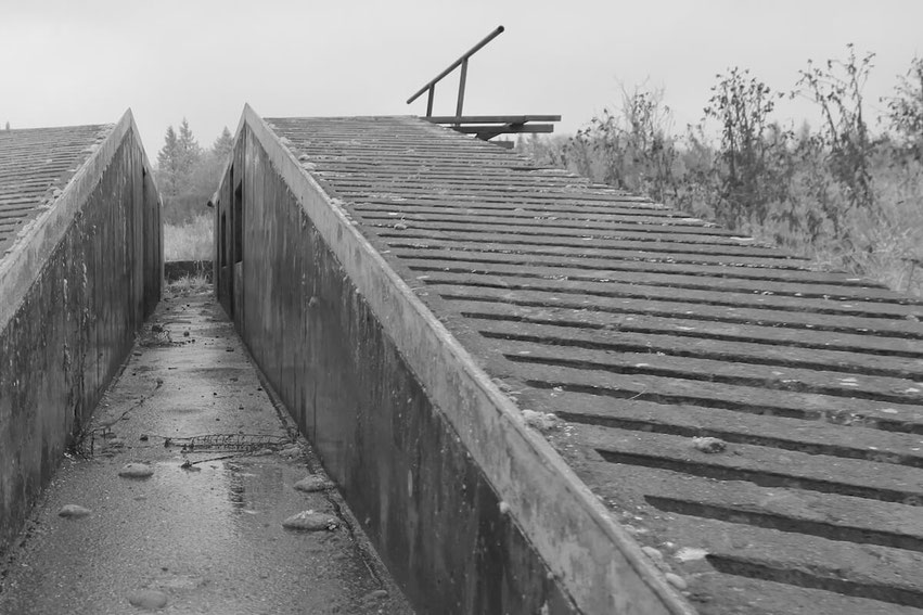 Das Schwarz-Weiß-Bild zeigt verwitterte Betonstrukturen eines ehemaligen Trainingsgeländes auf Camp Robertson, Schweinfurt, mit kühler, stillgelegter Atmosphäre.