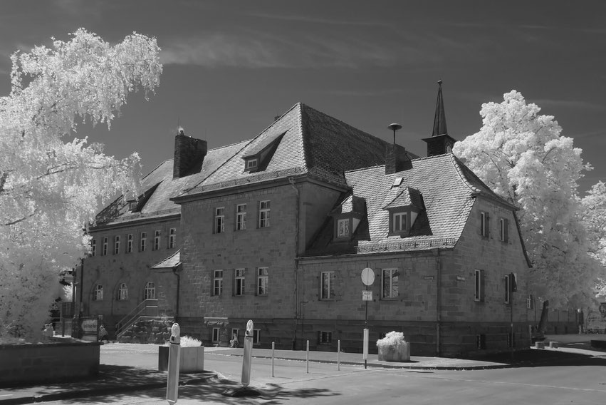 Das Gebäude der Schule in Zeil am Main zeigt sich als stattliches, mehrstöckiges Bauwerk mit traditioneller Architektur und kleinem Turm. Die Schwarz-Weiß-Infrarotaufnahme lässt die Bäume leuchtend weiß erscheinen.