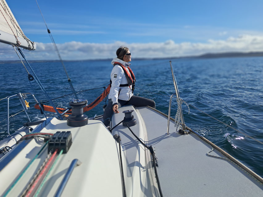 Skipper assise sur son voilier regardant la mer bleue et le Cap Sizun en Baie de Douarnenez.