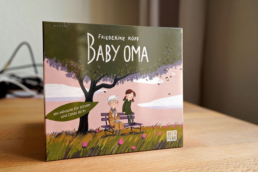 Die CD "Baby Oma" steht auf einem Tisch. Das Cover zeigt eine Oma und ihre Enkelin unter einem Baum.