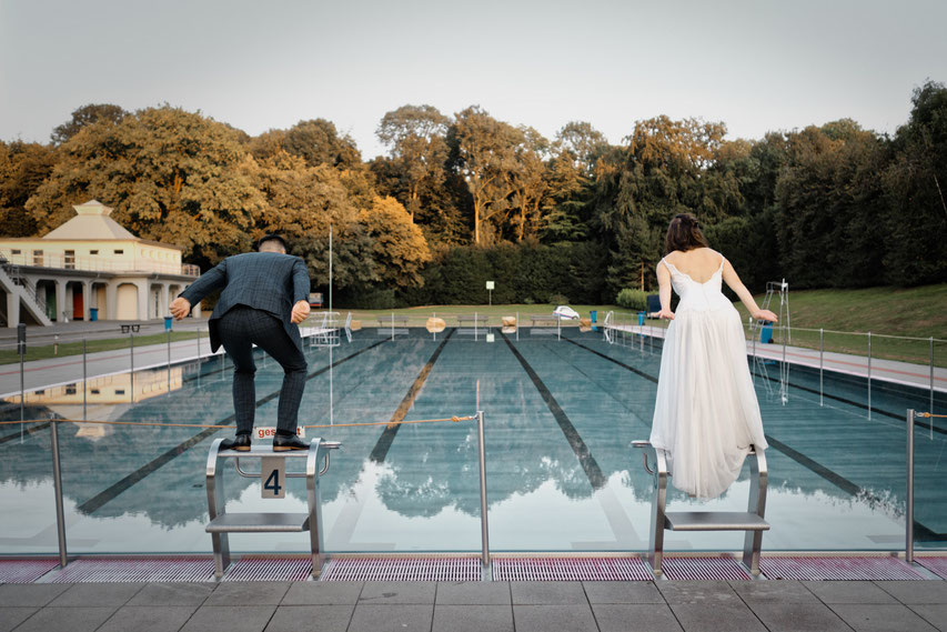 Ein Brautpaar tut so, als ob es gleich in ein Freibad springt.