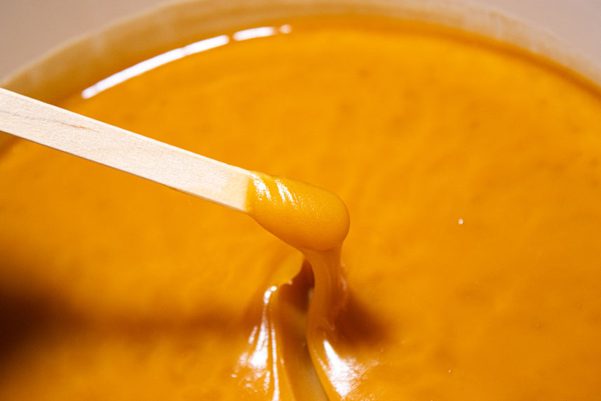 Miel de Rewarewa crémeux dans un seau de 10kg avec une touillette en bois faisant spiraler le Miel, la couleur est d'un orange vif, la texture est très onctueuse