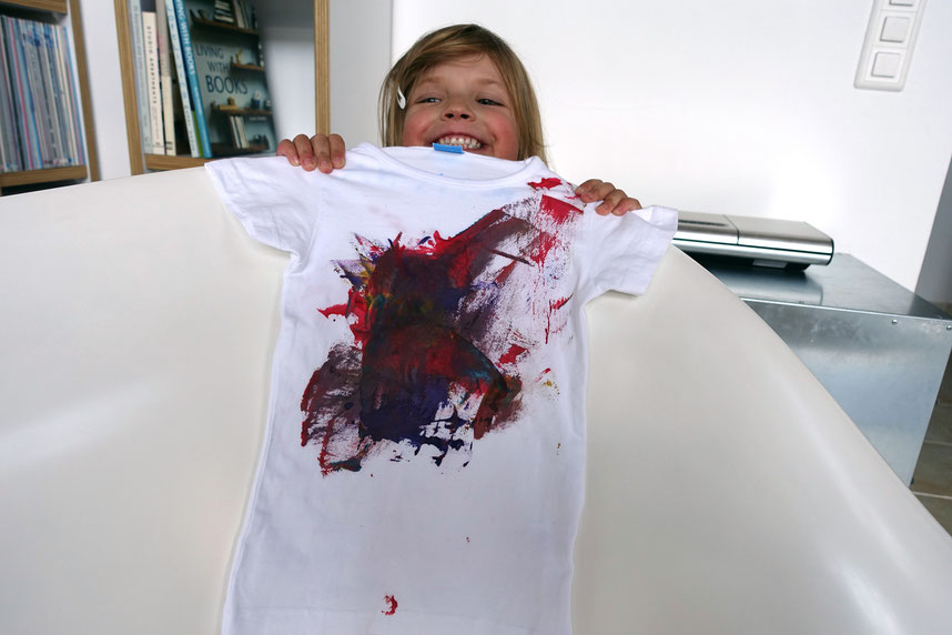 Kind zeigt Vorderseite eines mit Textilfarben bemalten weissen T-Shirts