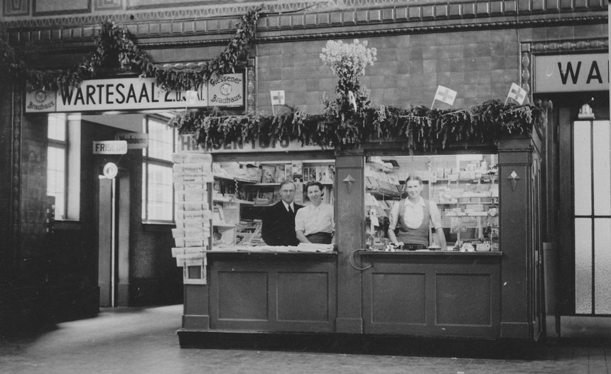 Kiosk im Bahnhof Bad Nauheim zwischen dem Wartesaal der 1., 2. und 3. Klasse um 1925; zu diesem Zeitpunkt beherbergte der Bahnhof auch einen Friseur, Waschräume und eine Gaststätte mit Bier vom "Giessener Brauhaus"