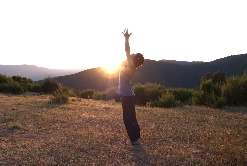 Personne pratiquant le yoga debout dans la nature, bras levés vers le ciel