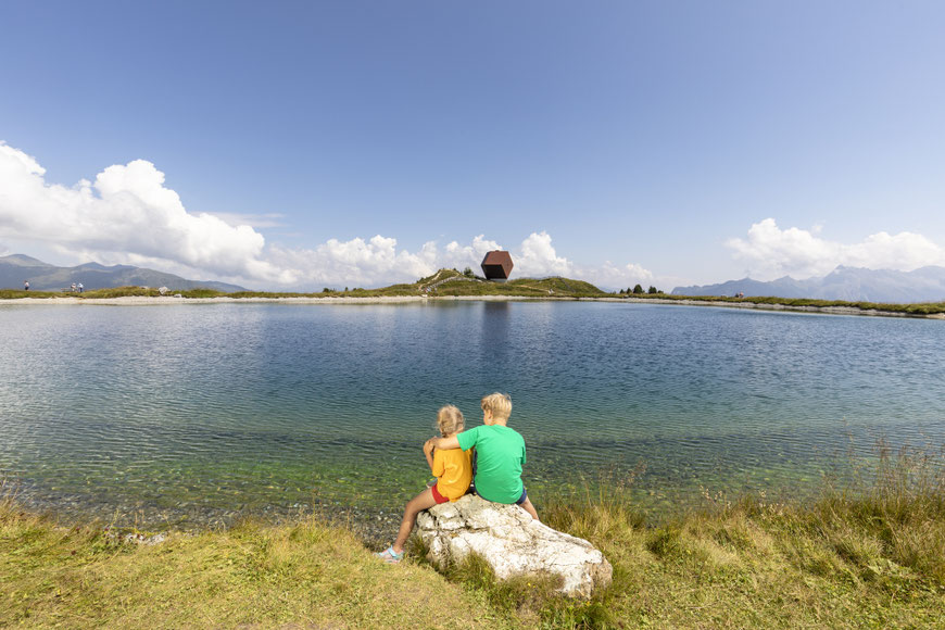 2 Kinder sitzen auf Stein vor Speichersee Penken - Ausgangspunkt Balthasarhof