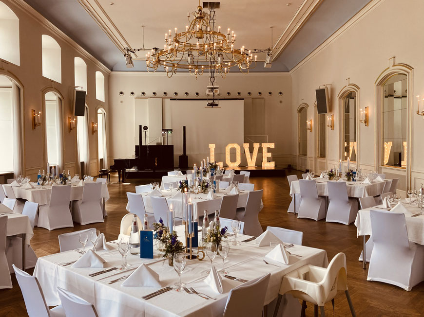 Festlich gedeckter Harmoniesaal in Bamberg mit Klavier und DJ-Equipment auf der Bühne – stilvolle Location für Hochzeit oder Event