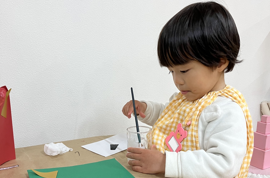 2歳児が、モンテッソーリの活動で、鬼のお面の製作でのりで貼る活動に集中して取り組んでいます。