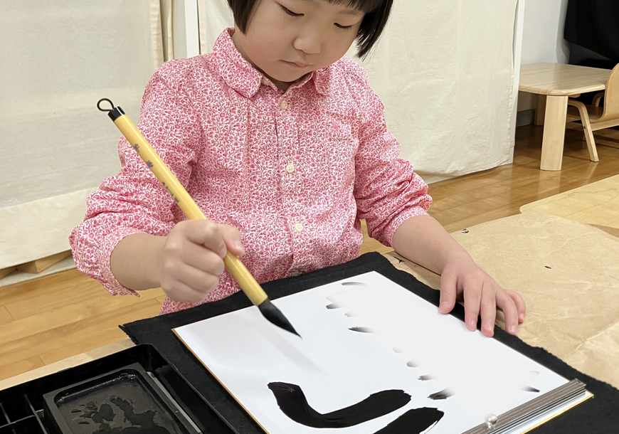 幼稚園児が、モンテッソーリの活動で書初めに集中して取り組んでいます。