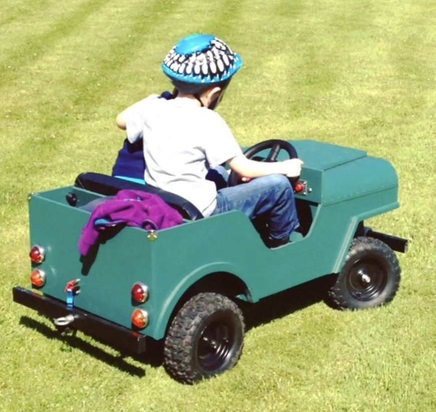 Handmade custom electric jeep inspired by Toylander plans driving across grass with two children riding inside