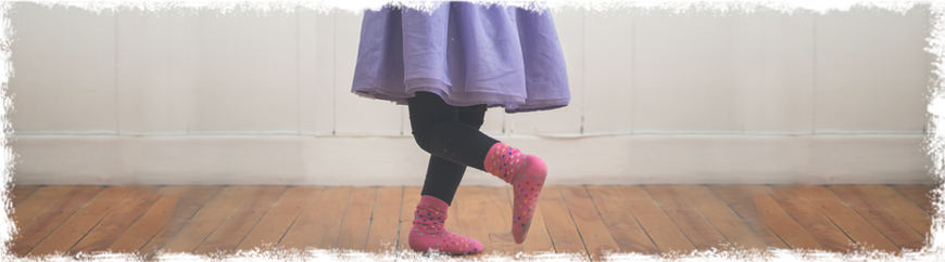 Kleines Mädchen mit pink Socken und lila Tütü tanzt auf einem Parkettboden, Glückskinder Hofheim