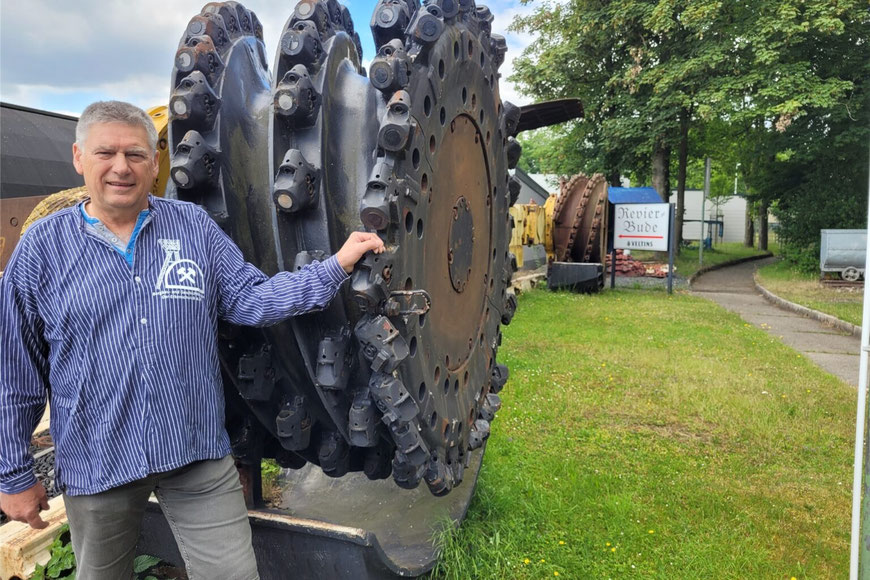 Volker Seemann, der 2. Vorsitzende des Bergbauvereins, zeigt auf dem Außengelände des Bergbaumuseums eine große Schrämmwalze, mit der einst die Steinkohle in einem Bergwerk im Saarland unter Tage herausgebrochen wurde © Jörg Müller