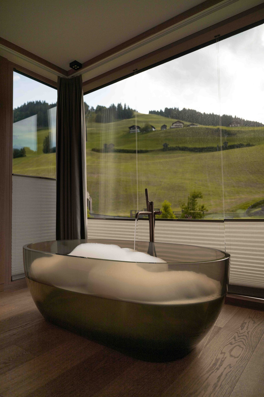 durchsichtige Badewanne vor einem großen Panoramafenster - NESSLERHOF in Großarl • 5-Sterne-Wellnesshotel im Salzburger Land