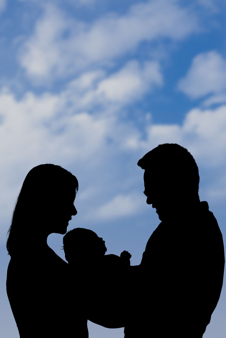 black and white silhouette of mother, new baby, and father against a blue sky with clouds