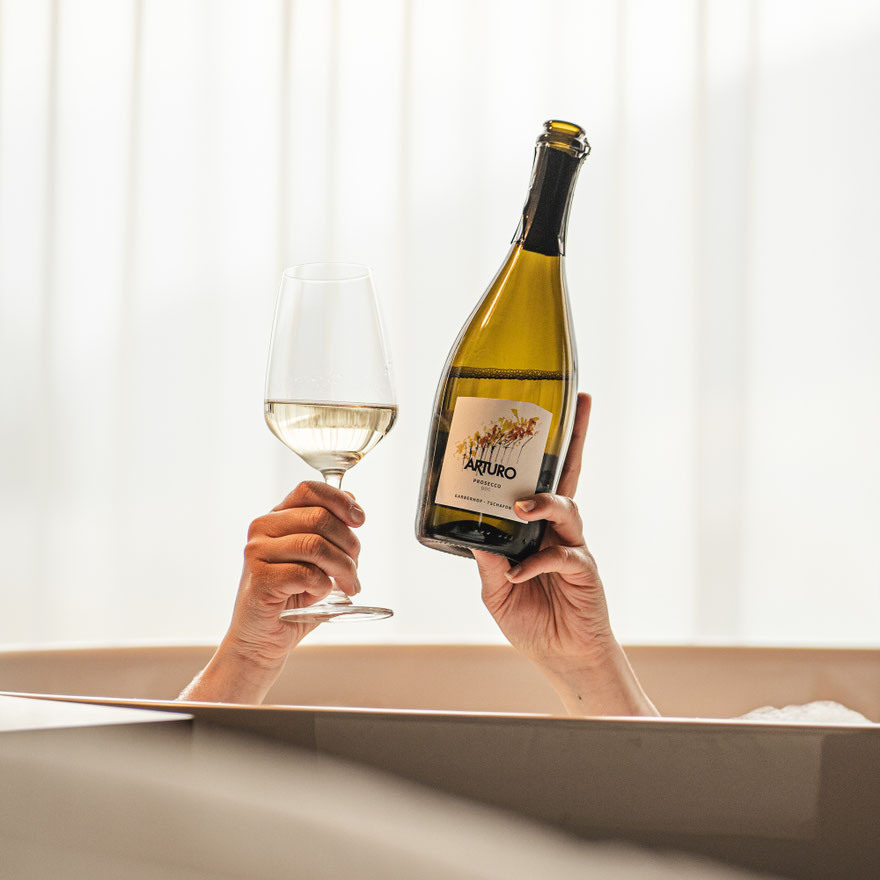 Ein Glas Prosecco und eine Flasche „Arturo“ des Garberhof werden entspannt aus einer Badewanne heraus gehalten.