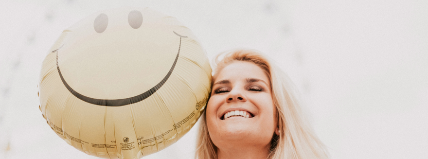 Lachende Frau mit Smiley-Ballon – Sinnbild für Leichtigkeit, Lebensfreude und positive Veränderung auf der Startseite von Feelglück Coaching