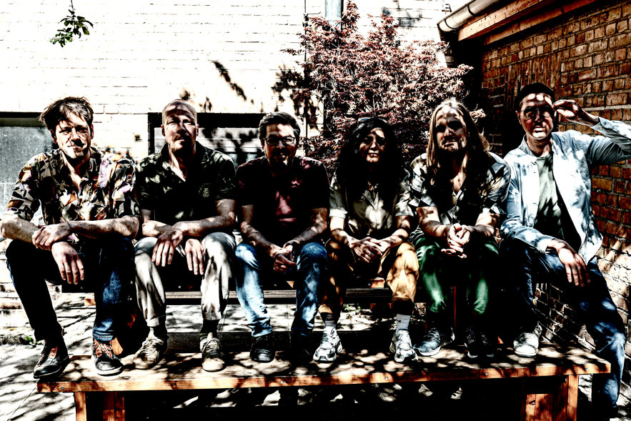 Die MusikerInnen der Band SADA sitzen auf einer Bank, Schattenspiele verfremden ihre Gesichter