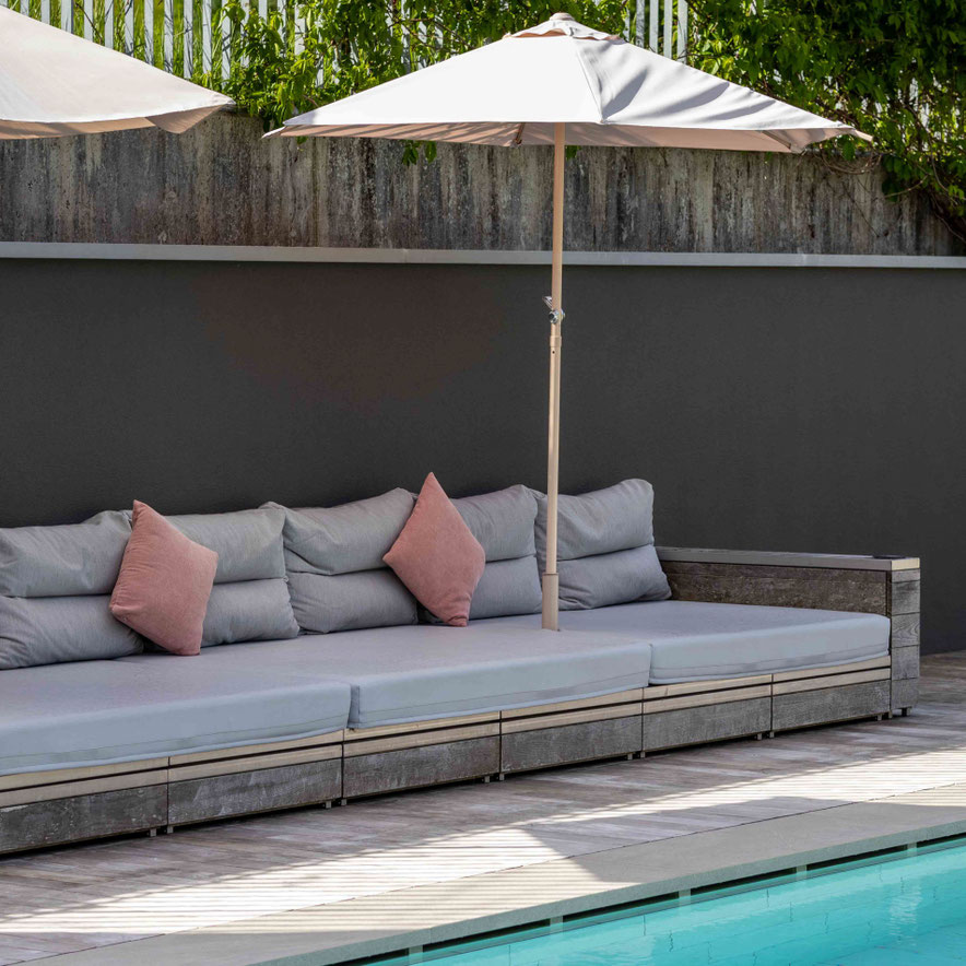 A comfortable lounge bench with parasols by the outdoor pool at the PETRUS boutique hotel in Reischach-Bruneck • South Tyrol, ideal for relaxing in a peaceful atmosphere.