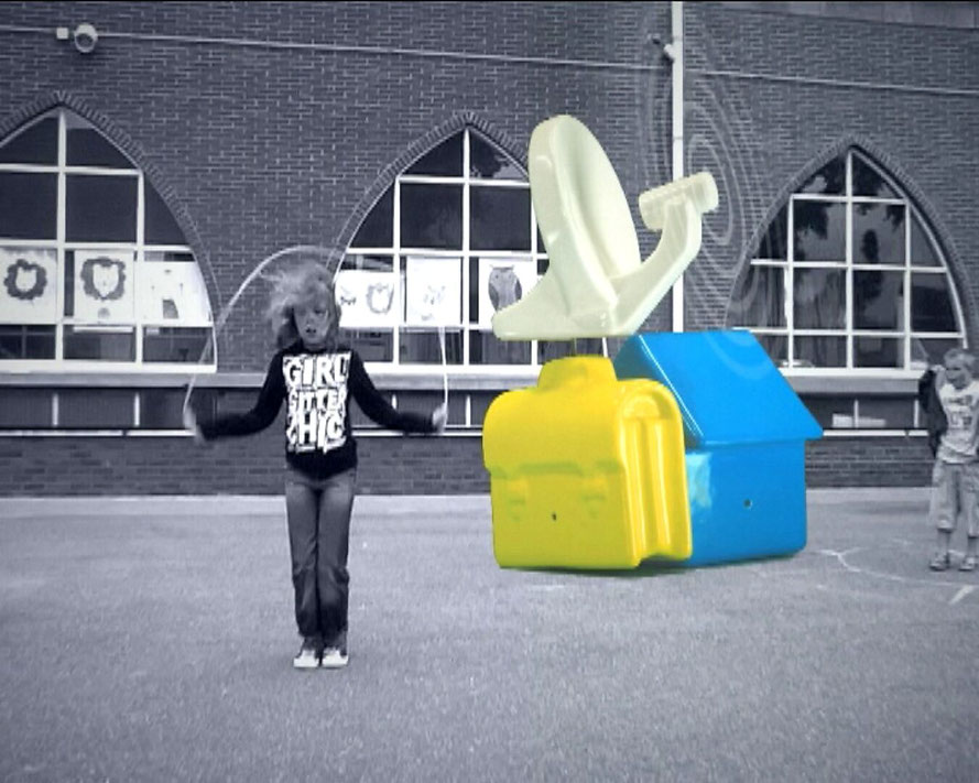 Ongeïdentificeerde Arcade — videostill met een springtouwend kind op een speelplaats voor een bakstenen gebouw, naast kleurrijke abstracte objectvormen.