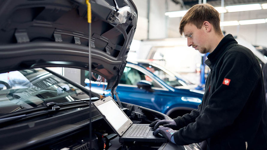 Ein Mitarbeiter des Autohaus Fischer untersucht die Motorhaube eines Autos,