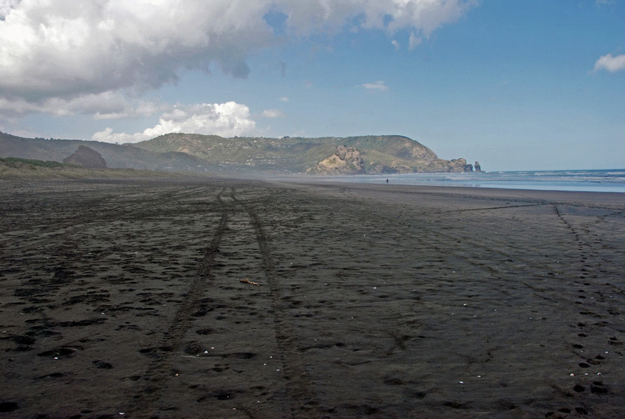 The vastness of Piha Beach at low tide from the north end, the Lion Rock on the left and the scruffy, pillowy blak sand stretching away to Taitomo Island and the Nun Rock. 