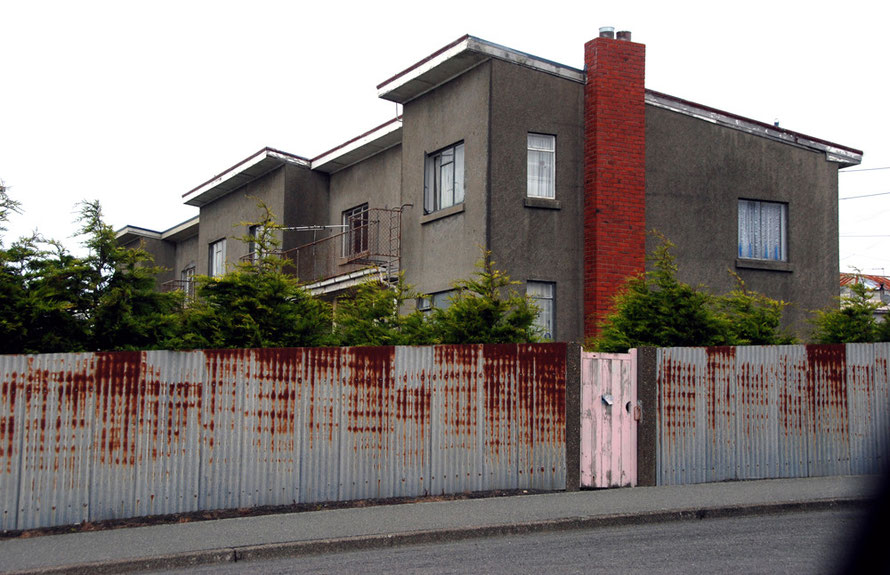 Pebbledashed low-rise apartments, corrugated iron fence and pink gate, East End, Bluff, Southland, NZ.