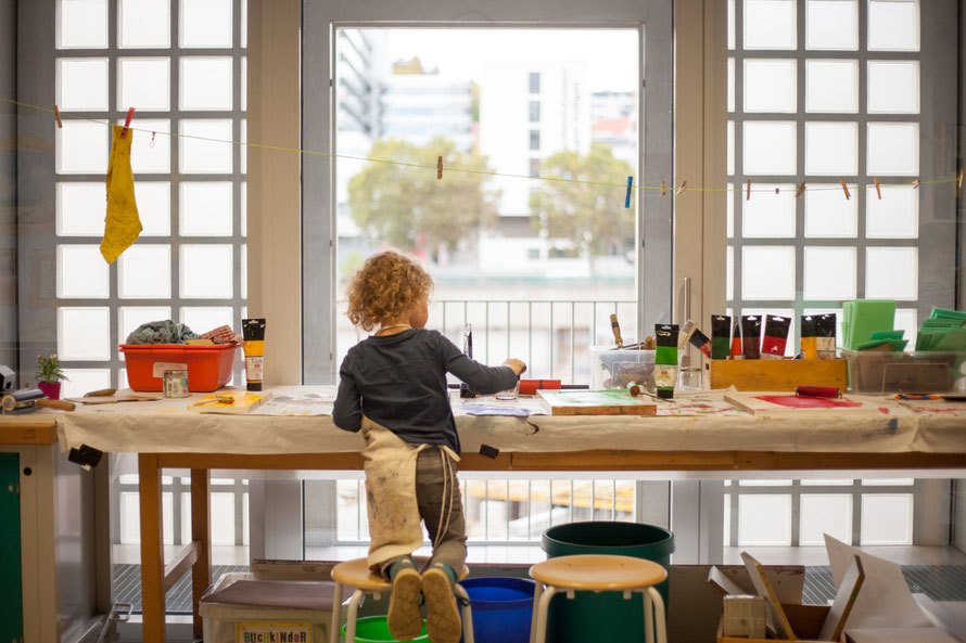 Drucktisch mit verschiedenen Farben, ein Kind walzt Farbe auf die Druckplatte