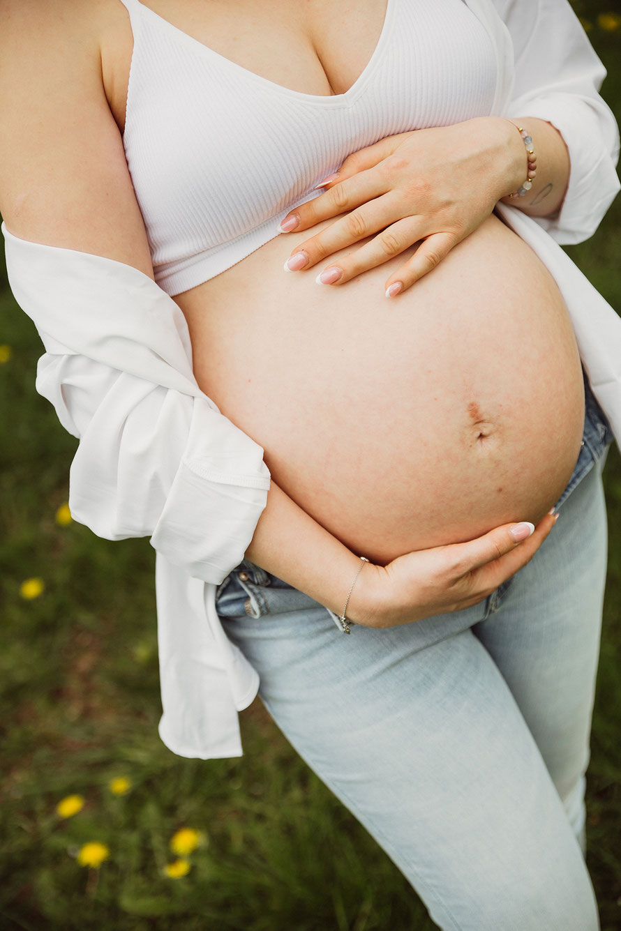 Nahaufnahme eines Babybauchs mit Händen der werdenden Mama – emotionale Schwangerschaftsfotografie in natürlicher Umgebung