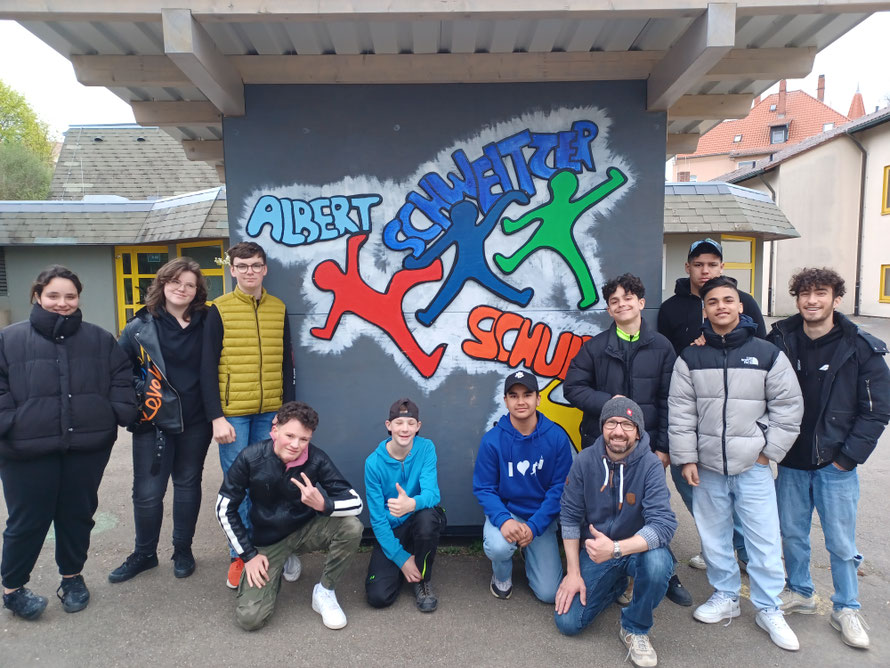 Das Bild zeigt 11 Schüler und ihren Lehrer vor ihrem Projekt, dem verkleideten Spielecontainer