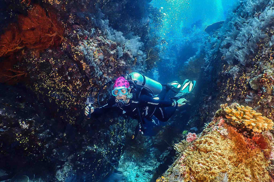 Scuba Diver in a swim-through with nice corals, holding a Gopro in El Nido, Palawan. Underwater Photography. Learn Scuba Diving.