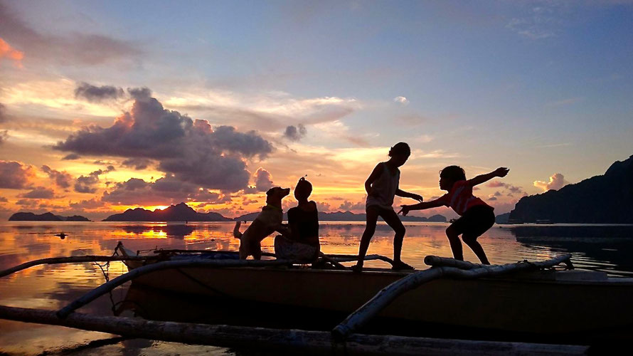 silhouettes of children and a dog on playing on a little boat. in the background a wonderful sunset near miniloc island, palawan
