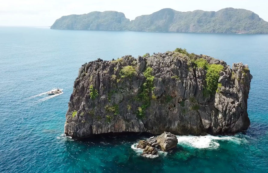 Drone shot of north rock, a famous dive site near El Nido. A bangka is driving by in the background.