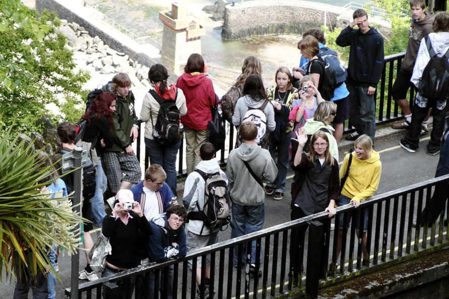 What's the story? Group of youths on a bridge. Most looking down on the harbour below or crossing over to do so. A few looking up/snapping/waving at the photographer making this picture. Who? No idea. Why? No idea. When? No idea.