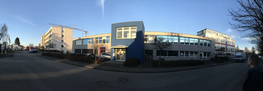 Gebäude (Aufnahme mit Fischaugenoptik) vor blauem Himmel. In der Mitte ein blauer Gebäudeteil mit Treppenhaus 