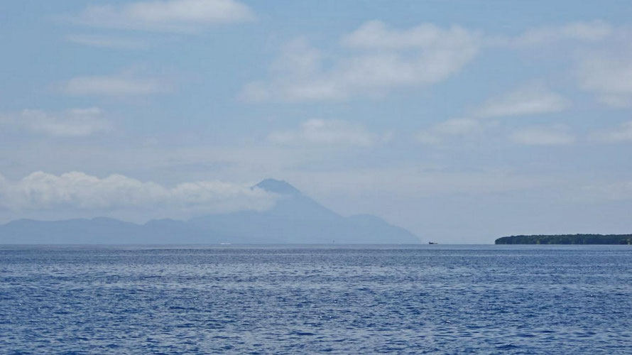 In der Ferne der aktive Vulkan vor der Insel Pama