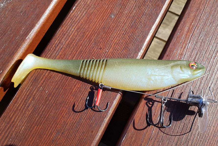 1. Anhalten des Arretierungsdrahtes am Gummifisch 2. Arretierungsdraht mittig durch den Köder stechen. Das Ende sollte ca. 3-8mm aus dem Köder austreten. 3. Fixierungsstifte in den Köder einstechen. 4. Arretierungshaken am Arretierungsdraht einhängen.