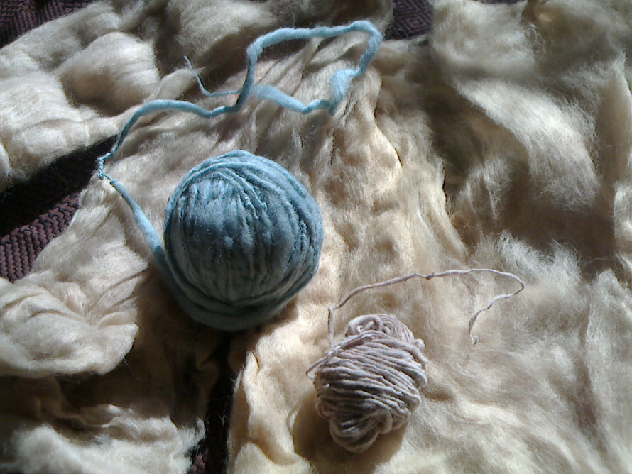 ウールの原毛の上に、左から藍染めのウールの手紡ぎ糸と、藍の紫染めの木綿の手紡ぎ糸です。