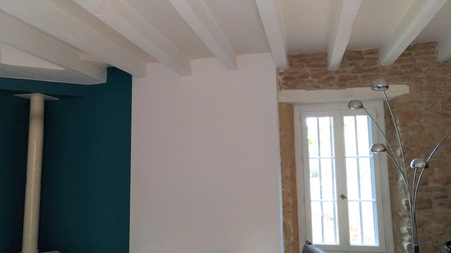 Intérieur avec pierres apparentes et poutres repeintes en blanc. Murs peints en bleu et poêle en céramique.