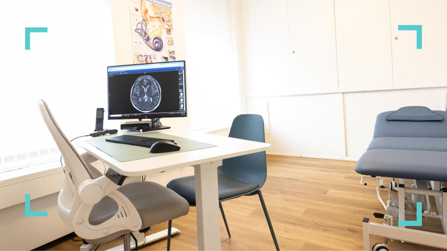 Foto der Praxis mit Behandlungszimmer, Monitor, Schreibtisch. Euro im Zentrum