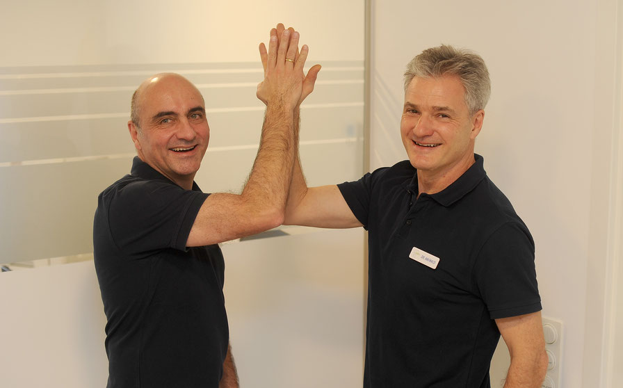 Die Zahnärzte Dr. Uwe Maiwald und Dr. Jens Staudenmayer aus Ludwigsburg geben sich lächelnd ein High Five in der Gemeinschaftspraxis Maiwald Staudenmayer